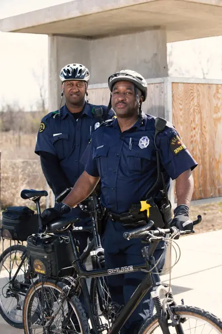 Portrait of Bicycle Police officers standing outside with their bikes looking towards camera smiling 