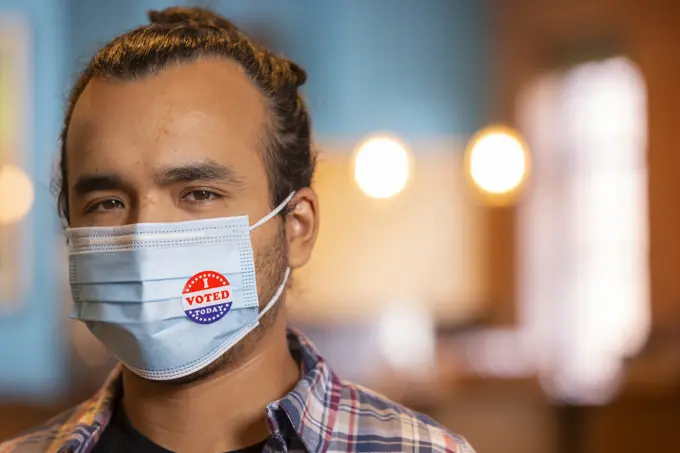 Indoor portrait of a Hispanic male wearing a mask and an I Voted Today sticker on the mask