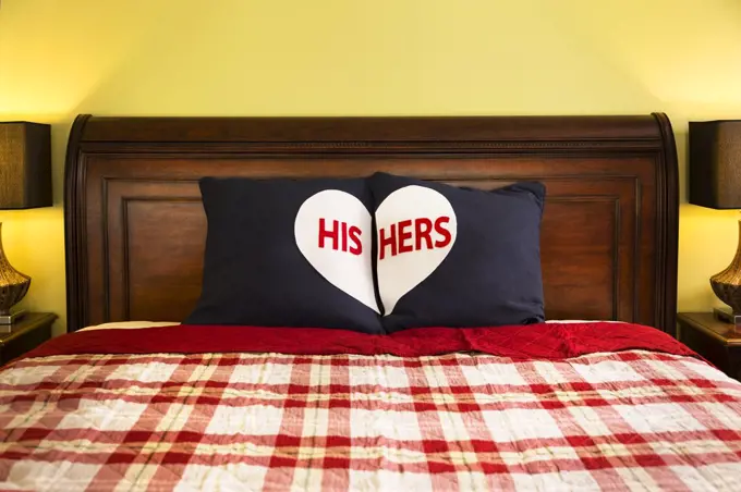 Detail shot of decorative His and Hers Pillows on dark wooden sleigh bed with red and white plaid comforter in master bedroom of home 