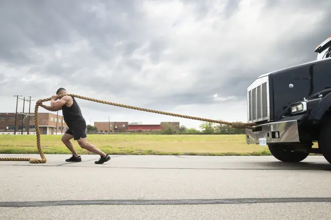 Muscular Hispanic man wearing tank top, Pulling semi truck with large tow rope 