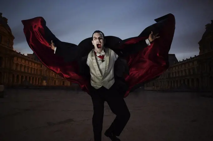 Count Dracula showing fangs and holding his cape out while running towards the camera at night