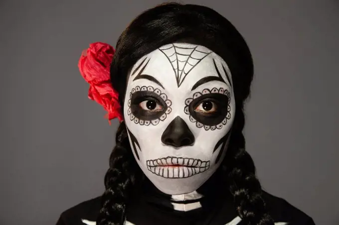 Portrait of a woman dressed up in for Halloween and Day of the Dead Dia de los Muertos with skull face paint. Looking into camera.