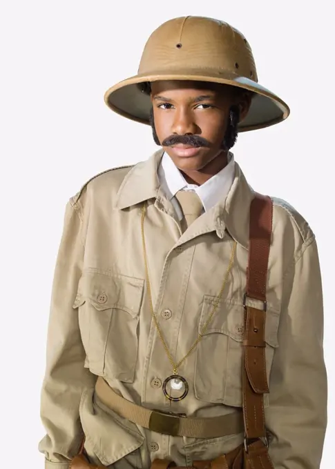 Portrait of a boy dressed up as archaeologist mummy hunter  with a fake mustache and sideburns looking into camera, against a white background 