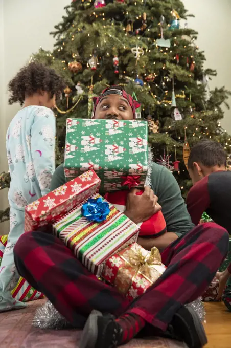 Man playing with his family in front of Christmas tree.