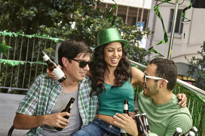 Woman sitting on laps on friends while celebrating St. Patrick's day outside drinking beer.