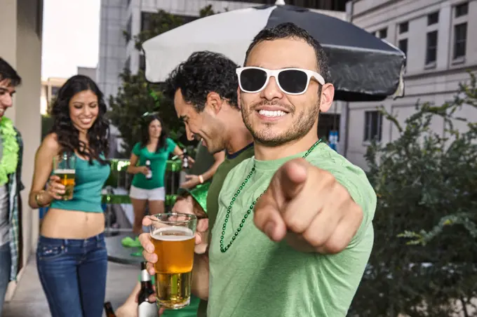 Portrait of a man pointing at camera while holding a beer glass at party for St Patrick's Day.