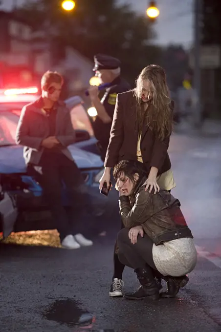 Injured young women on the sceen of an automobile accident , police officer talking with young man in background 