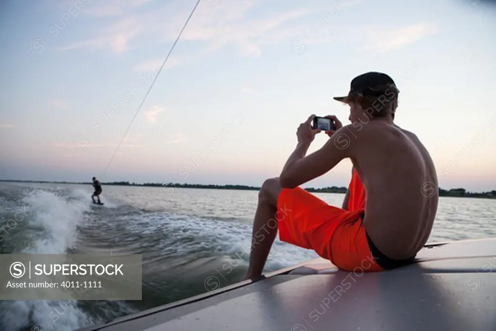 Teenager recording video of friend wakeboarding from back of boat