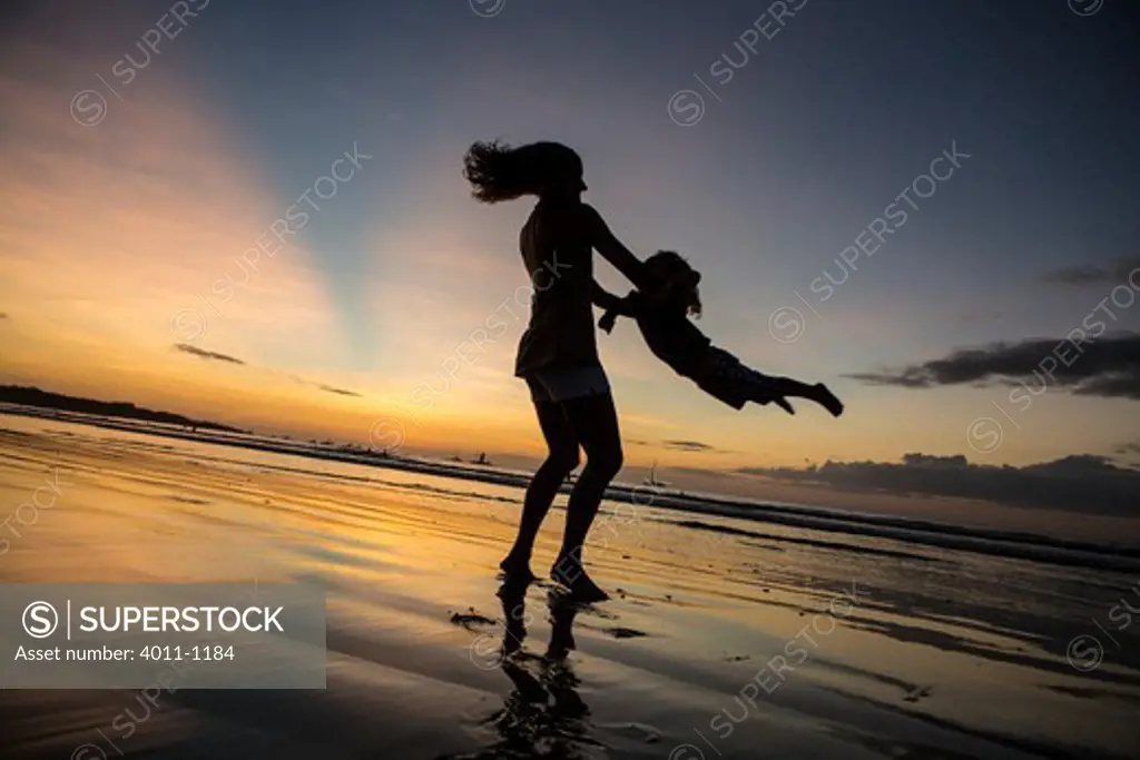 Woman swinging her daughter on the beach at sunset, Costa Rica