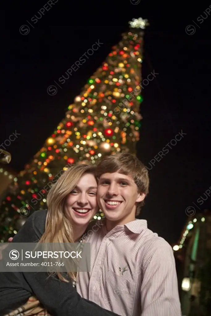 Teenage couple standing in front of a Christmas tree and smiling