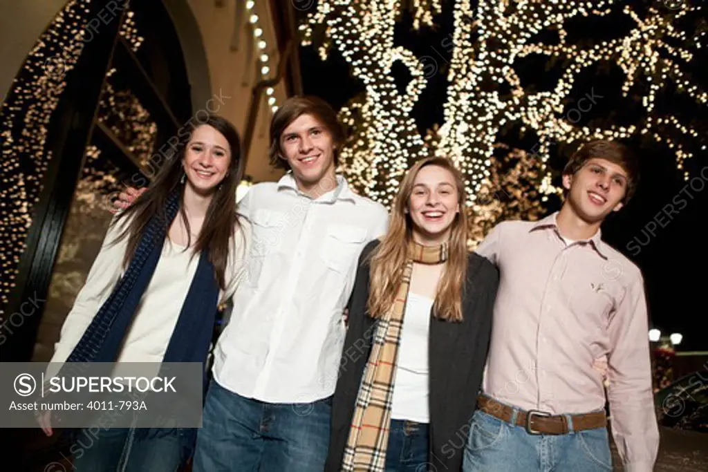 Four teenage friends standing in front of a Christmas tree and smiling