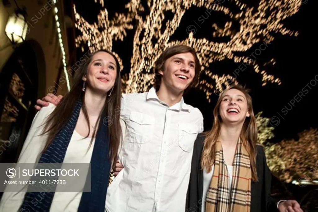 Teenage friends standing in front of a Christmas tree and smiling