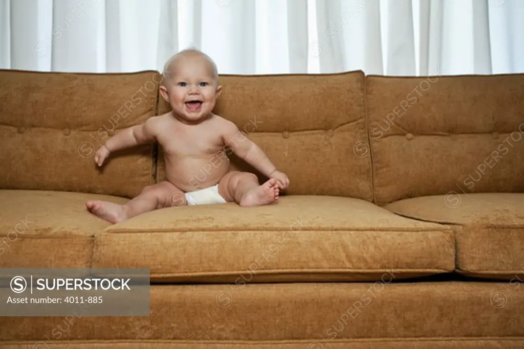 Seven month old baby on couch wearing diaper and laughing