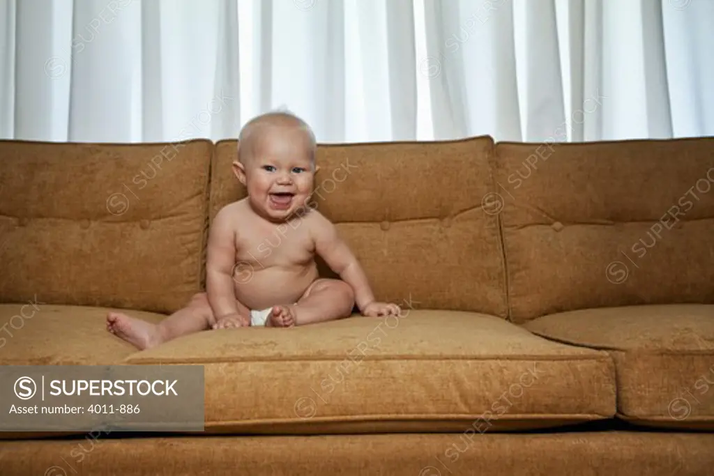 Seven month old baby on couch wearing diaper and laughing