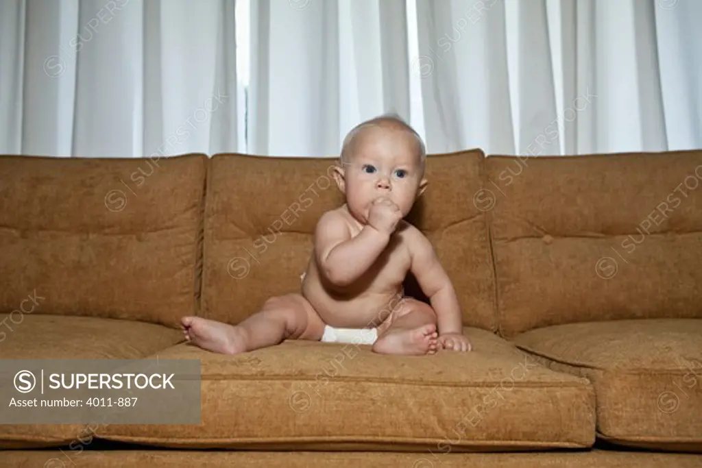 Seven month old baby on couch wearing diaper with thumb in mouth