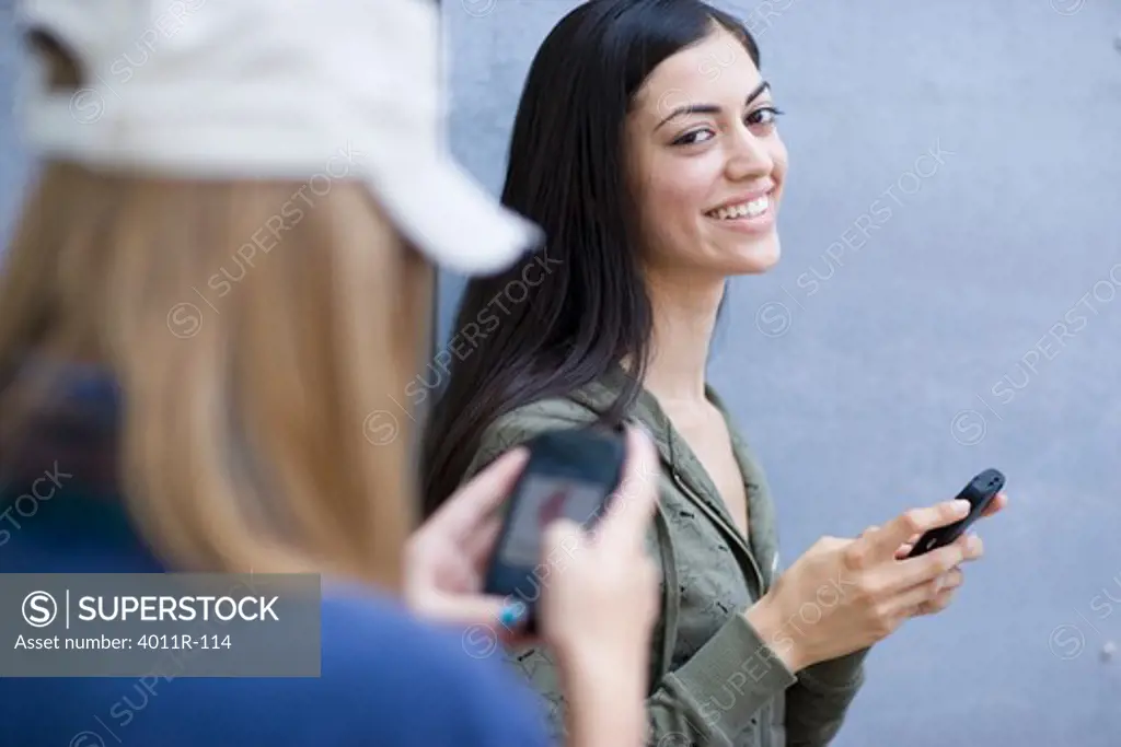 Two female friends text messaging on mobile phones