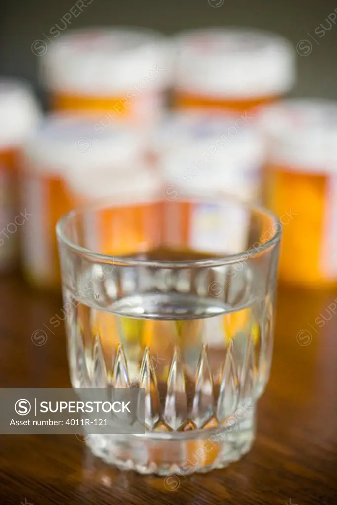 Glass of water with pill bottles in the background
