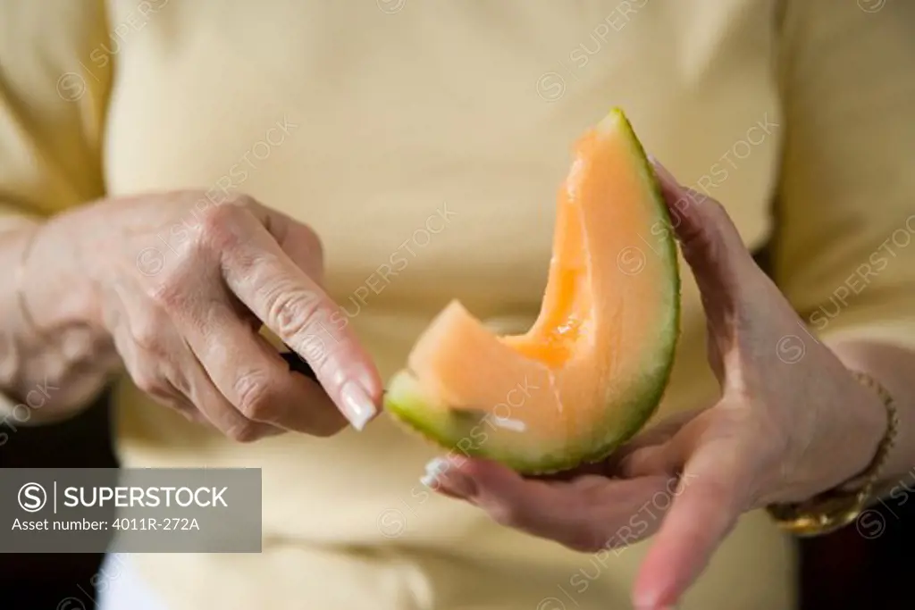 Close up of elderly woman's hands cutting cantaloupe