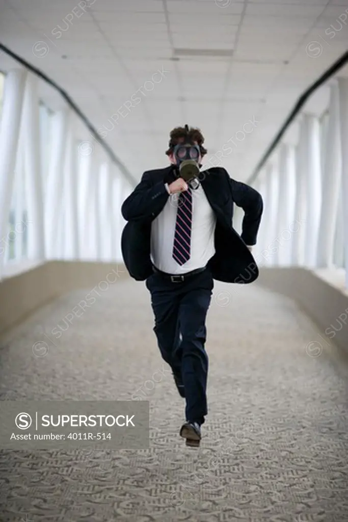 Businessman wearing gas mask running down corridor