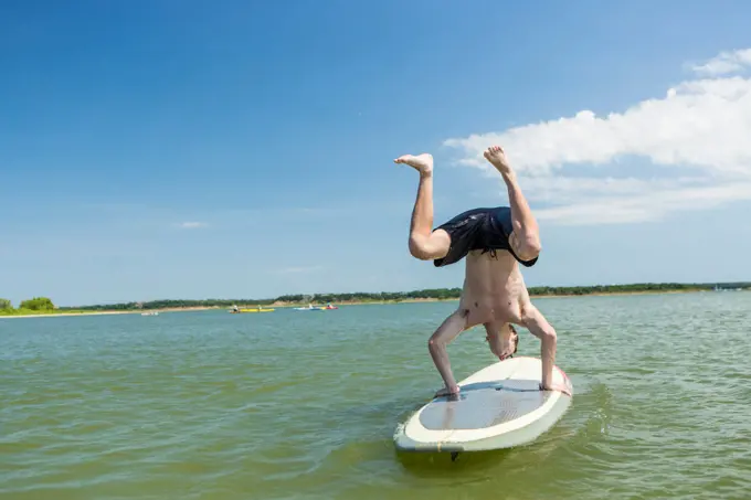 Caucasian boy doing handstand on paddleboard