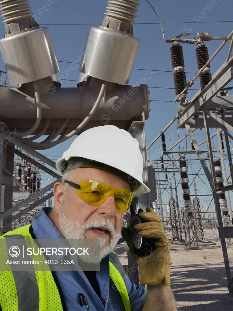 Engineer talking on a walkie-talkie in front of large transformers at a power station