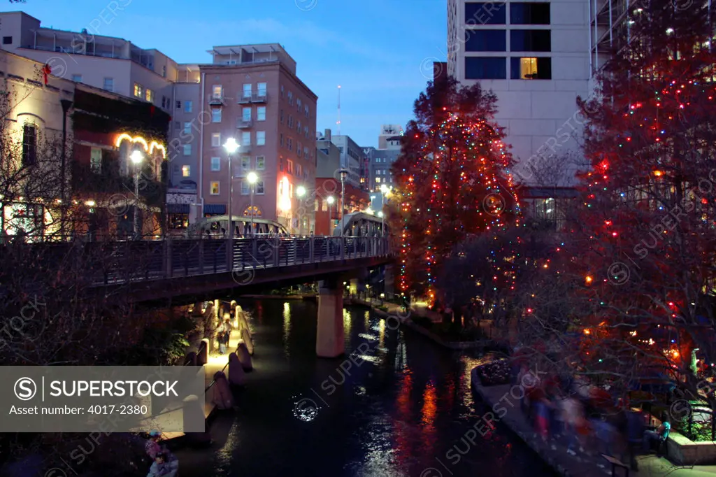 San Antonio Riverwalk at Dusk with Lighted trees on the side of the River and a Pedestrian Bridge in the background