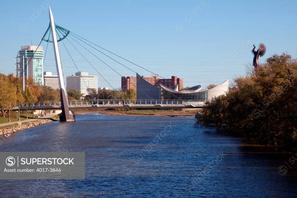 USA, Kansas, Wichita, Riverfront Pedestrian Bridge over Arkansas River with Keeper of Plains sculpture on right