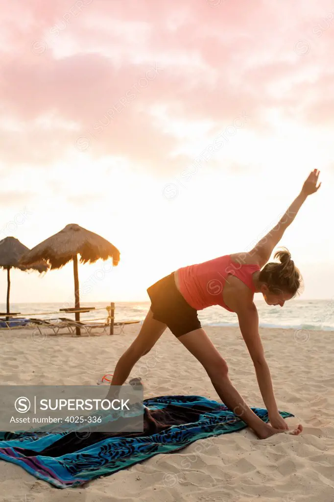 Mexico, Playa del Carmen, Young woman practicing yoga on beach at sunrise