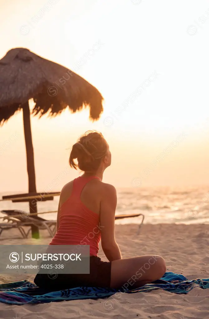 Mexico, Playa del Carmen, Young woman practicing yoga on beach at sunrise