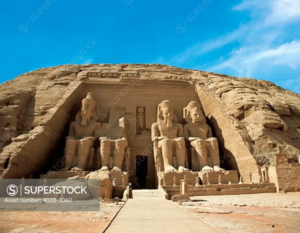 Egypt, Abu Simbel, The Greater Temple of Ramses II, Colossal statues of King Ramesses II near Lake Nasser, Man walking on grounds in the early morning.
