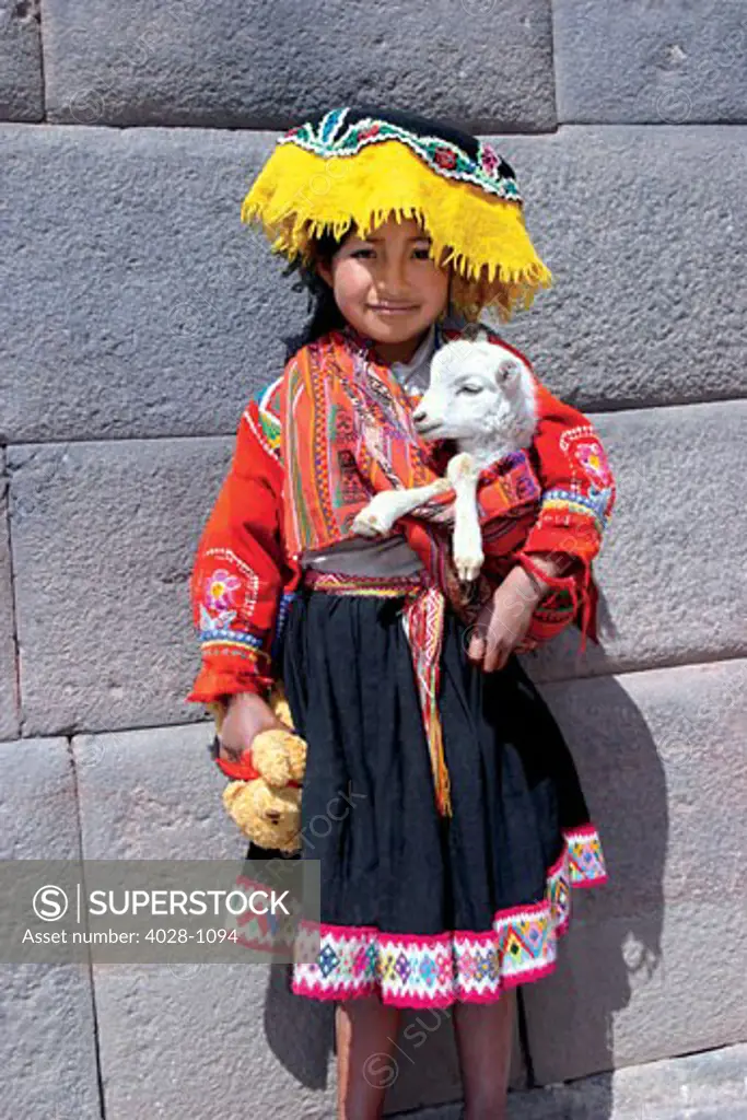 Cusco, Peru, A local girl dressed in traditonal clothing poses with her pet goat or lamb in the Sacred Valley of Peru in the city of Cusco at a local market.