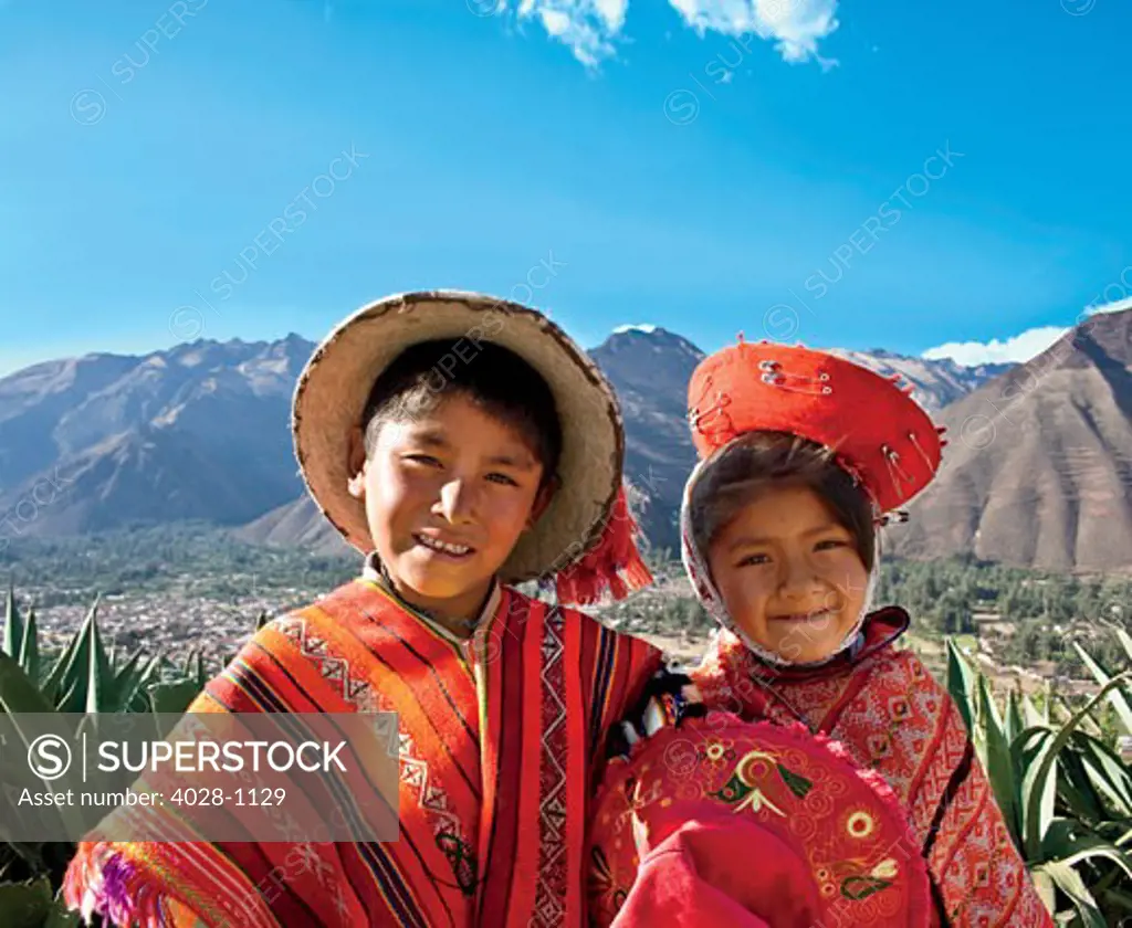Cusco, Peru, A local boy and girl dressed in traditonal clothing pose while their family sells their wares at a local market above the Sacred Valley.