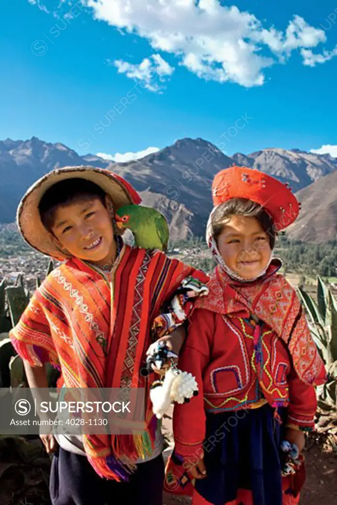 Cusco, Peru, A local boy and girl dressed in traditonal clothing pose with their pet parrot as their family sells their wares at a local market above the Sacred Valley.