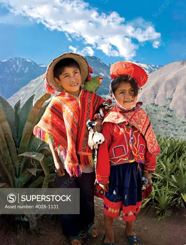 Cusco, Peru, A local boy and girl dressed in traditonal clothing pose with their pet parrot as their family sells their wares at a local market above the Sacred Valley.