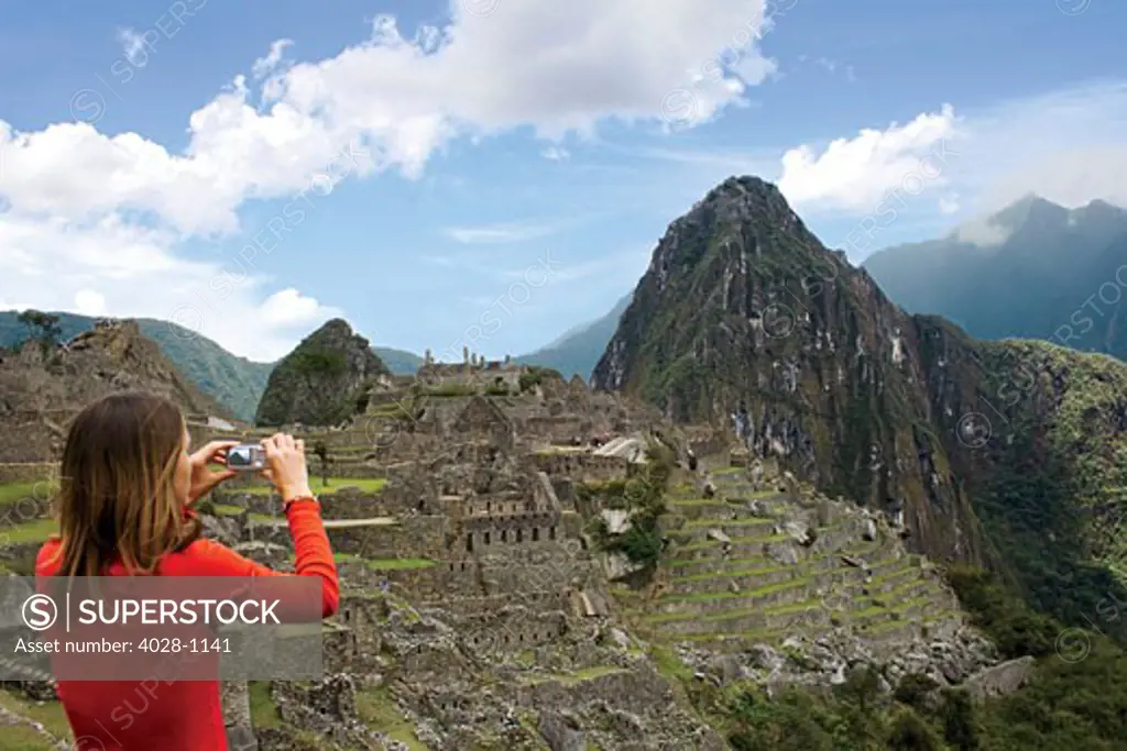 Peru, Machu Picchu, Woman takes a photograph overlooking the ancient lost city of the Inca.