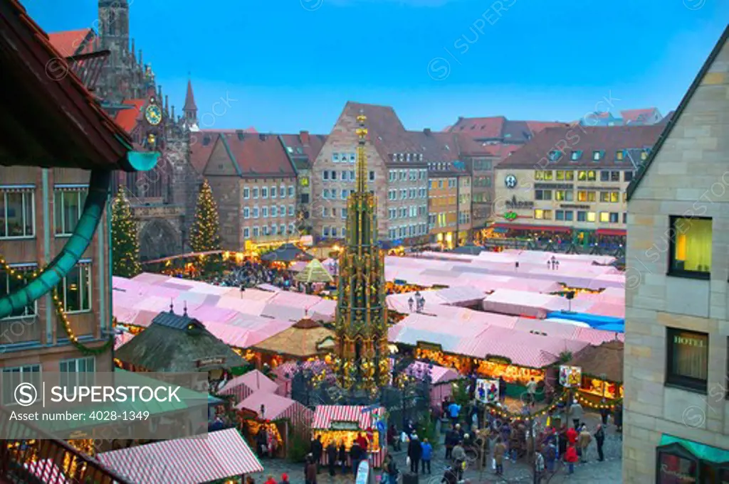 The Christmas Market of Nuremberg, Germany between Schoner Brunnen Fountain and Our Lady's Church at dusk.