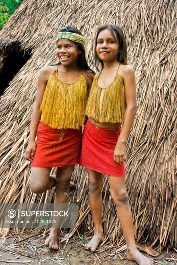 Two young girls stand outside of their tribal hut in the Peruvian Amazon Jungle near Iguitos, Peru