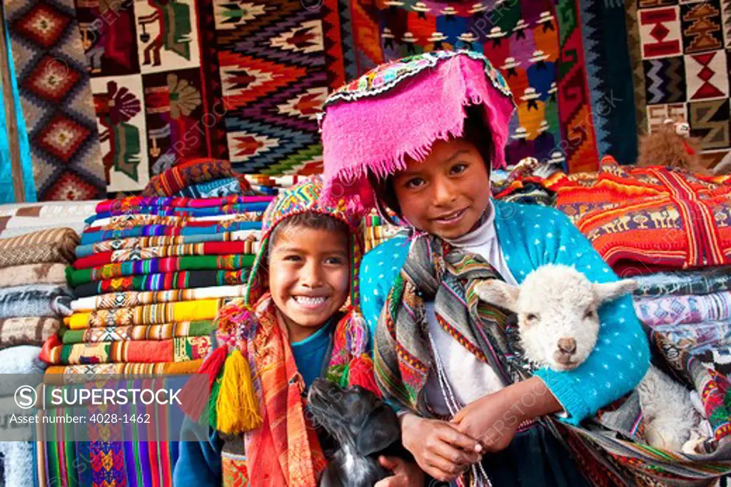 Pisac, Peru, A local boy and girl dressed in traditonal clothing pose with their pet goat or lamb and puppy in the Sacred Valley of Peru in the town of Pisac at a local market.
