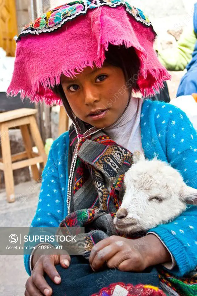 Pisac, Peru, A local girl dressed in traditonal clothing pose with her lamb as her family sells their wares at a local market in the Sacred Valley.