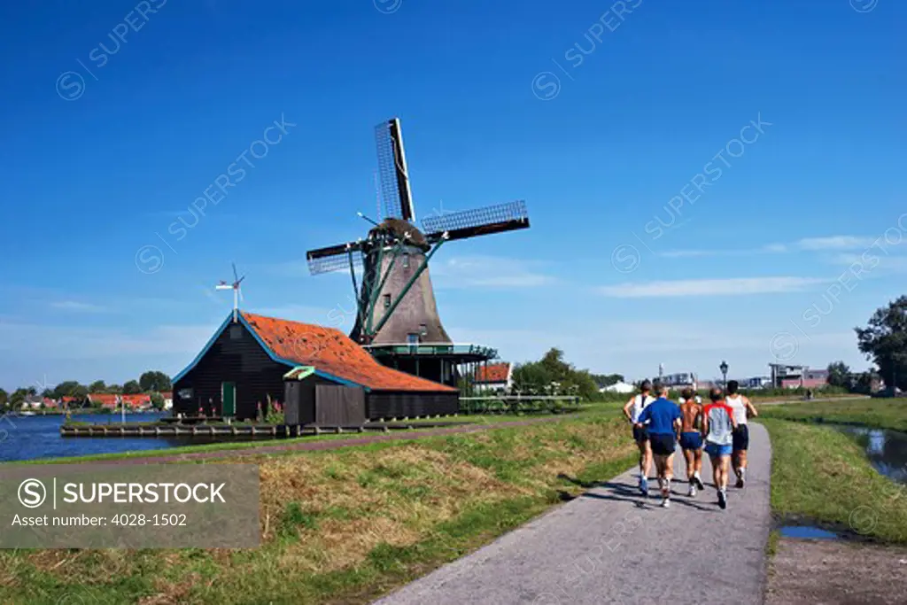 Netherlands, North Holland, Zaanstad, Zaanse Schans, windmills, Joggers on pathway along the canal.