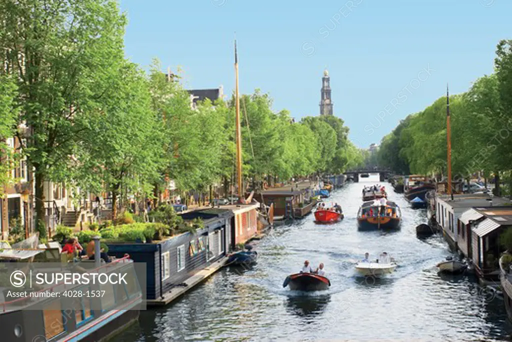 Netherlands, Amsterdam, Boats cruise along a canal with the Zuiderkerk bell-tower in the background. Holland.