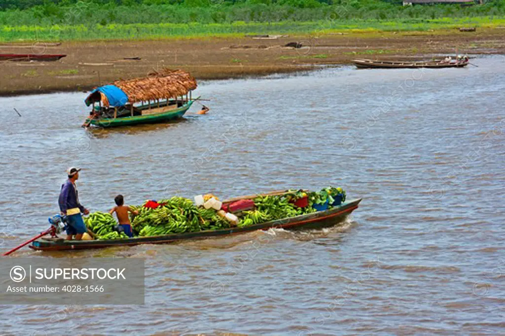 A boat carrying bananas floats in front of a village along the Amazon River of Peru or Brazil