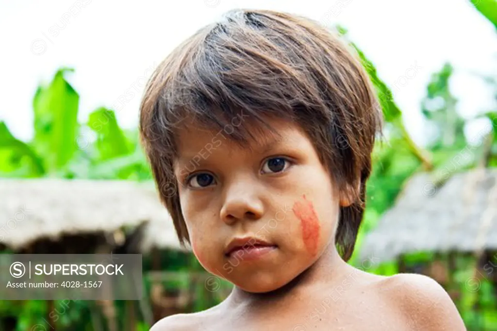 A young boy in face paint stand outside of their tribal hut in the Peruvian Amazon Jungle near Iguitos, Peru