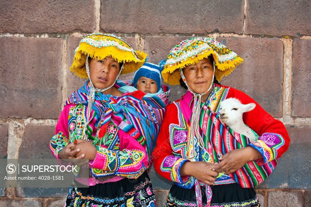 Cusco, Peru, Local women, one with a baby in her scarf, dressed in traditional clothing pose near the Cusco Cathedral in Cusco, Peru