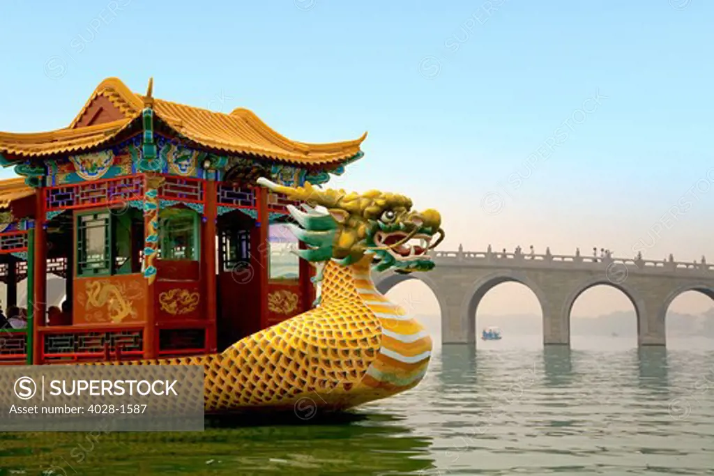 The Summer Palace, Beijing, China, a traditional Dragon Boat passes the Seventeen Arch Bridge as it takes tourists around the Kunming lake at the Emperor's Summer Palace in Beijing, China