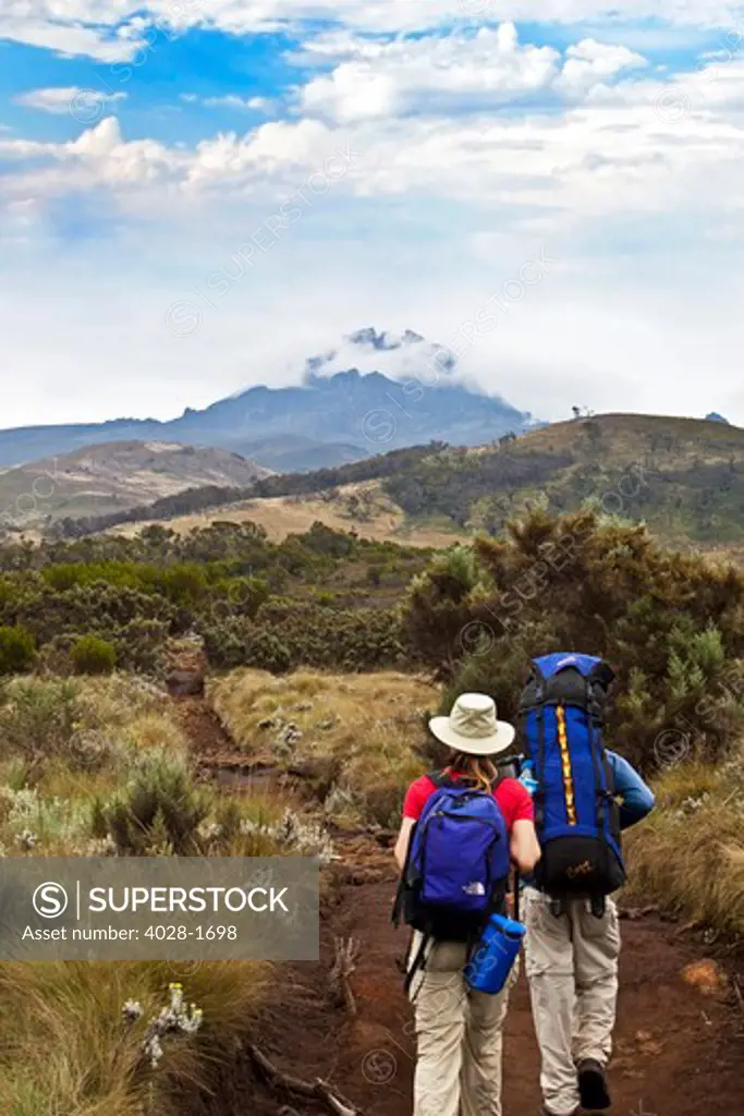 A man and a woman with backpacks hiking up the Marangu Route of Mt. Kilimanjaro, Tanzania