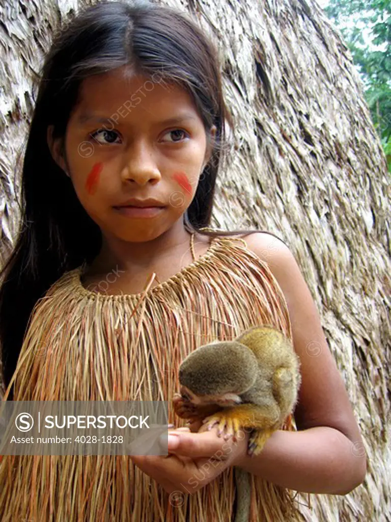 Young girl poses outside of her tribal village hut with a baby Capuchin monkey in the Peruvian Amazon Jungle near Iguitos, Peru.