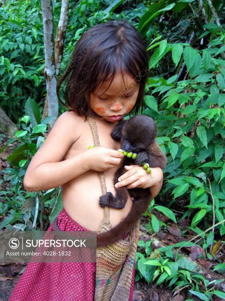 Young girl poses outside of her tribal village hut with a baby black Spider monkey in the Peruvian Amazon Jungle near Brasilia, Brazil
