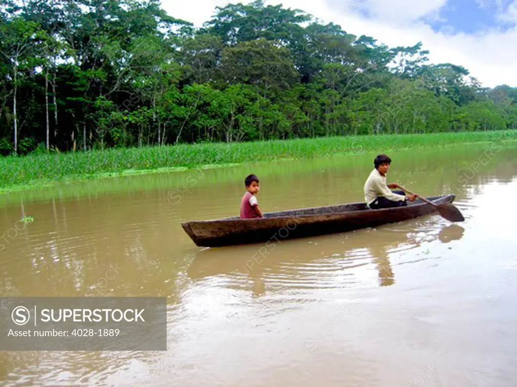 Two native boys paddle a canoe down the Amazon River in Brazil