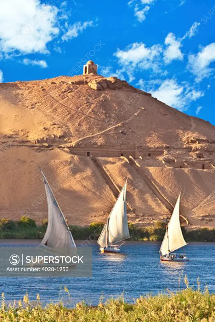 Egypt, Aswan, Nile River, Felucca sailboats, temple ruins and the large sand dunes of the Sahara Desert in the background.
